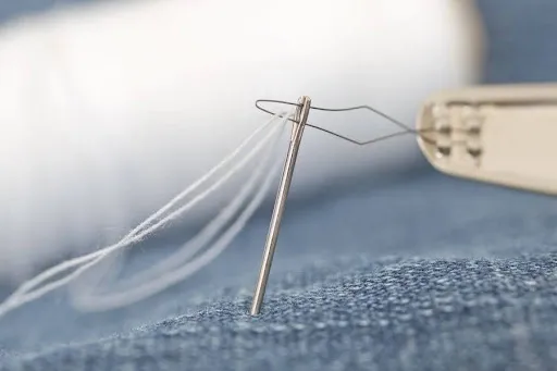 A denim needle and strong thread sewing a patch onto a denim jacket in close-up macro detail